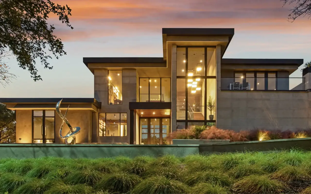 Contemporary custom home with stone walls and tall windows, lit at dusk