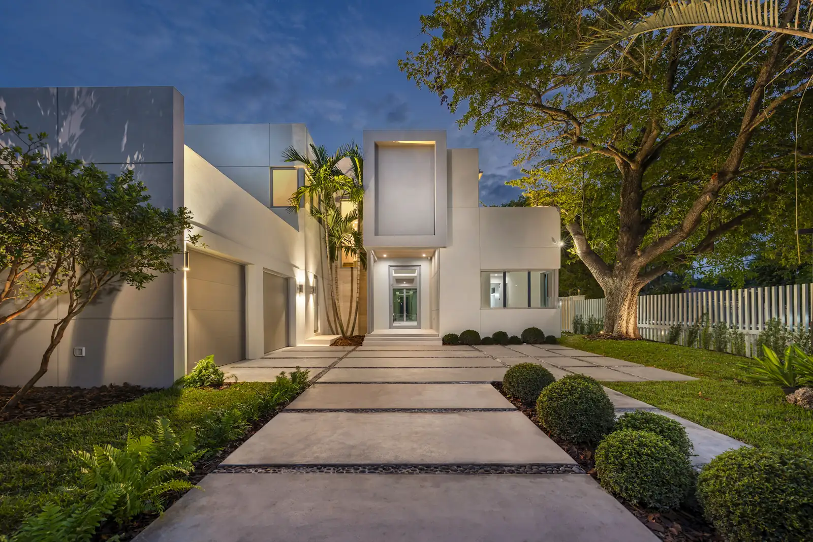 White modern home with flat roofs and a lit front walk at dusk